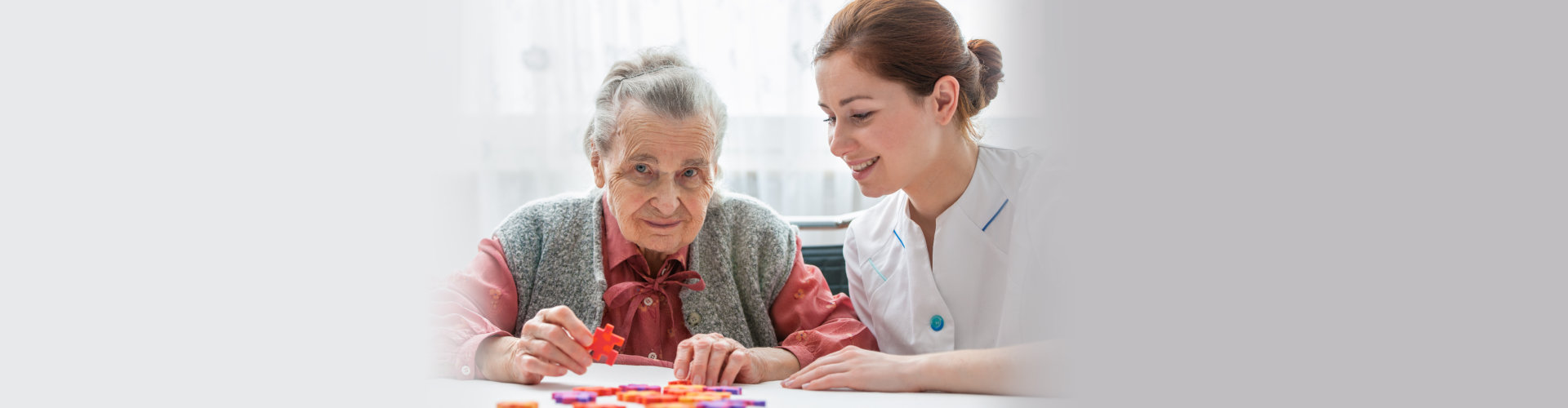 nurse playing jigsaw puzzle with senior woman in nursing home
